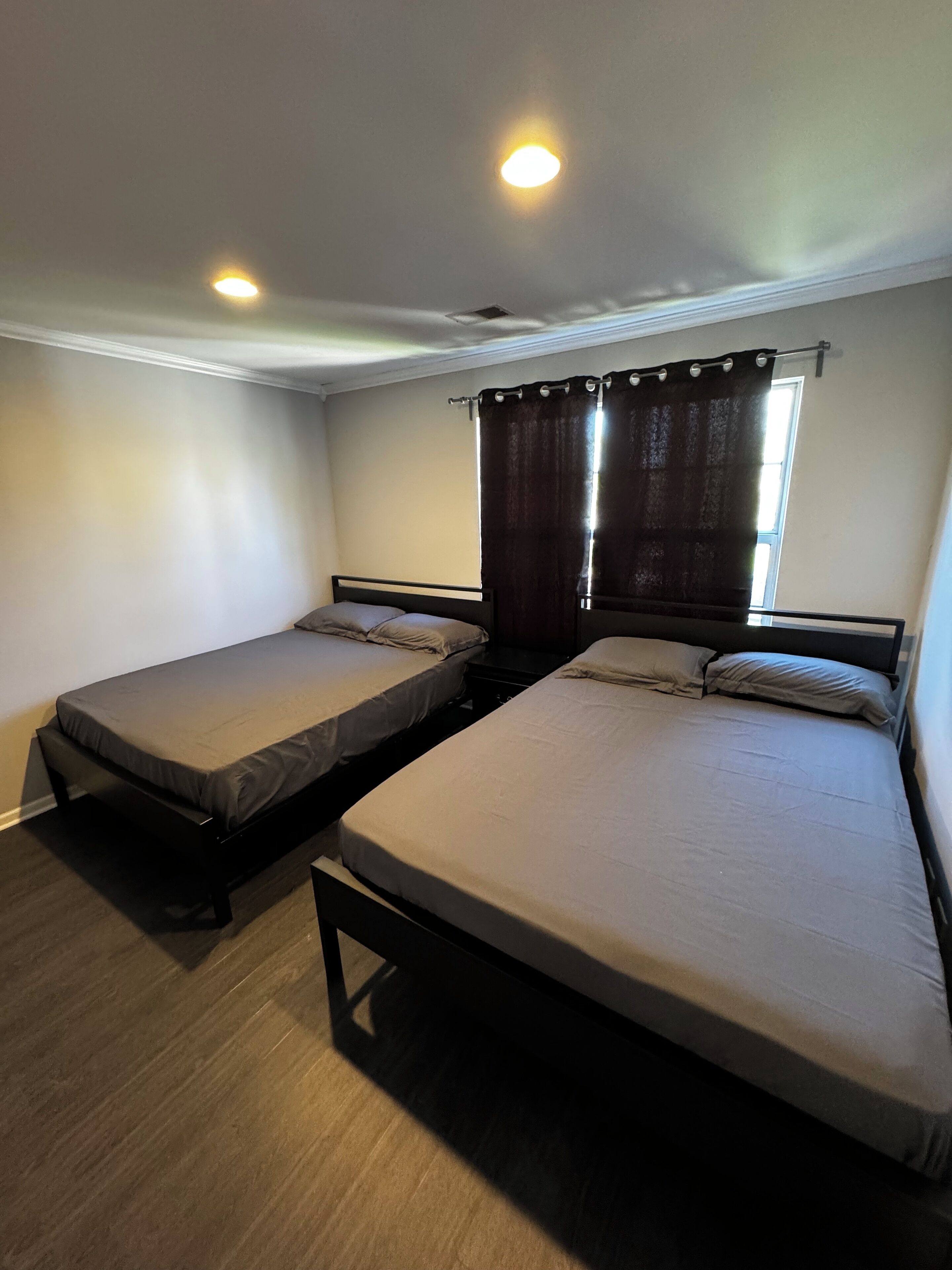 Quarto com duas camas de solteiro, janela com cortinas e uma luminária no teto.