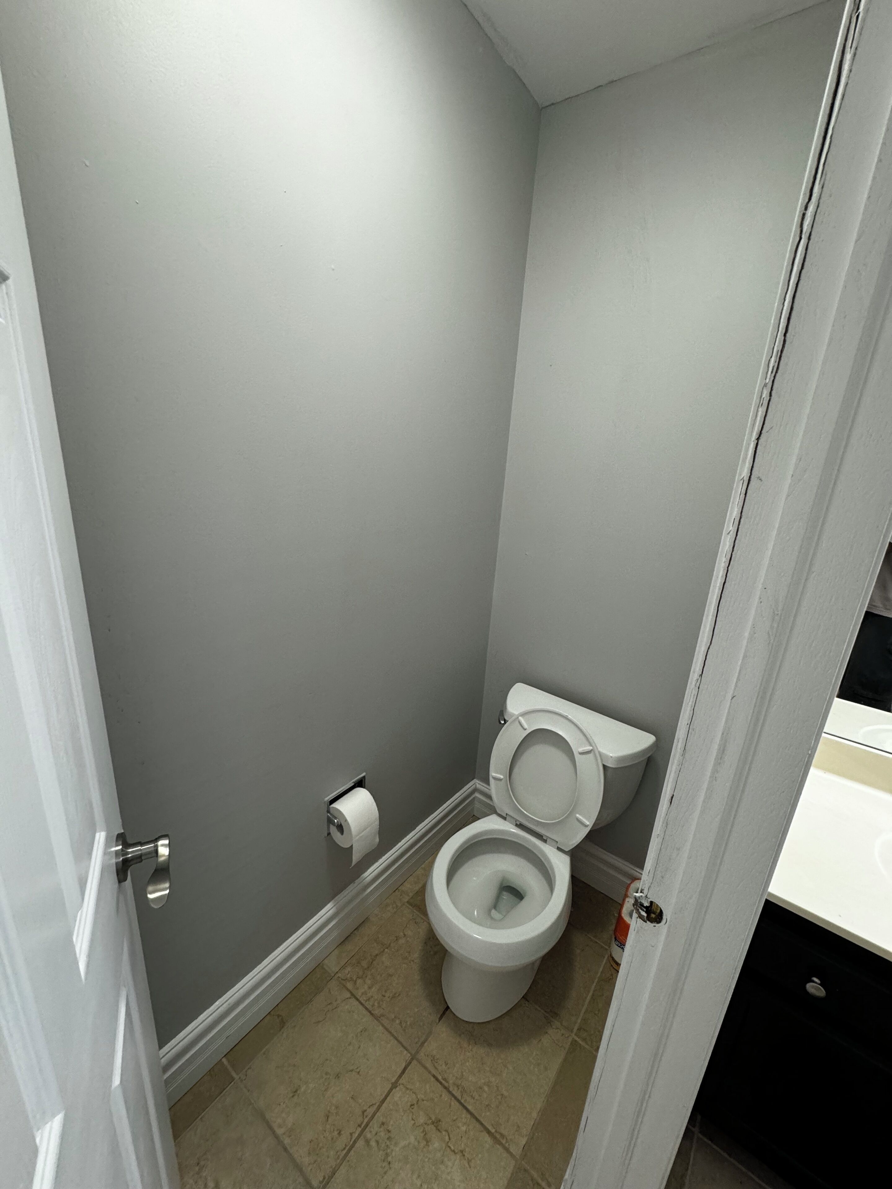 Ein kleines, schmales Badezimmer mit Toilette, einer Toilettenpapierrolle und beige gefliestem Boden.