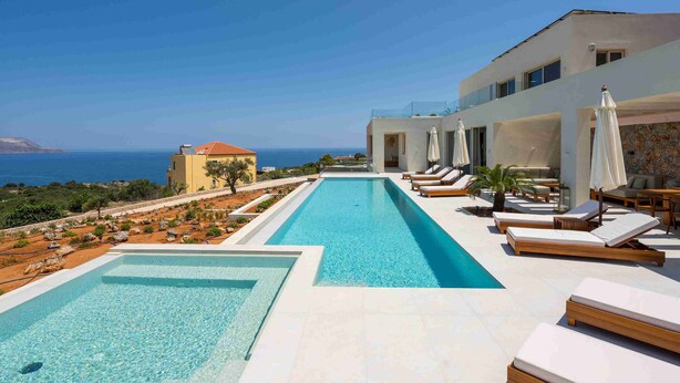 Une piscine dotée de chaises longues et de parasols, offrant une vue sur un paysage côtier.