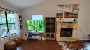 A living room with a fireplace, a television, and a dog lying on a rug. - Cowboy Pool Oasis (Bastrop)