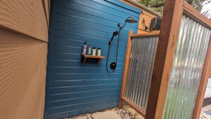 A blue exterior wall with a wooden shelf holding toiletries. - Cowboy Pool Oasis (Bastrop)