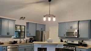 A kitchen with blue cabinets, a stainless steel refrigerator, a microwave, a stove, and two bar stools. - Cowboy Pool Oasis (Bastrop)