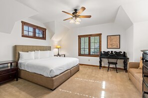A bedroom with a bed, a desk, a chair, a dresser, a ceiling fan, and two windows.