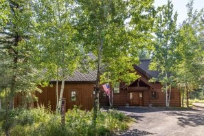 A rustic wooden cabin with a sloped roof, surrounded by dense greenery and a clear sky. - Charming Chalet on the Golf Course (Tamarack)