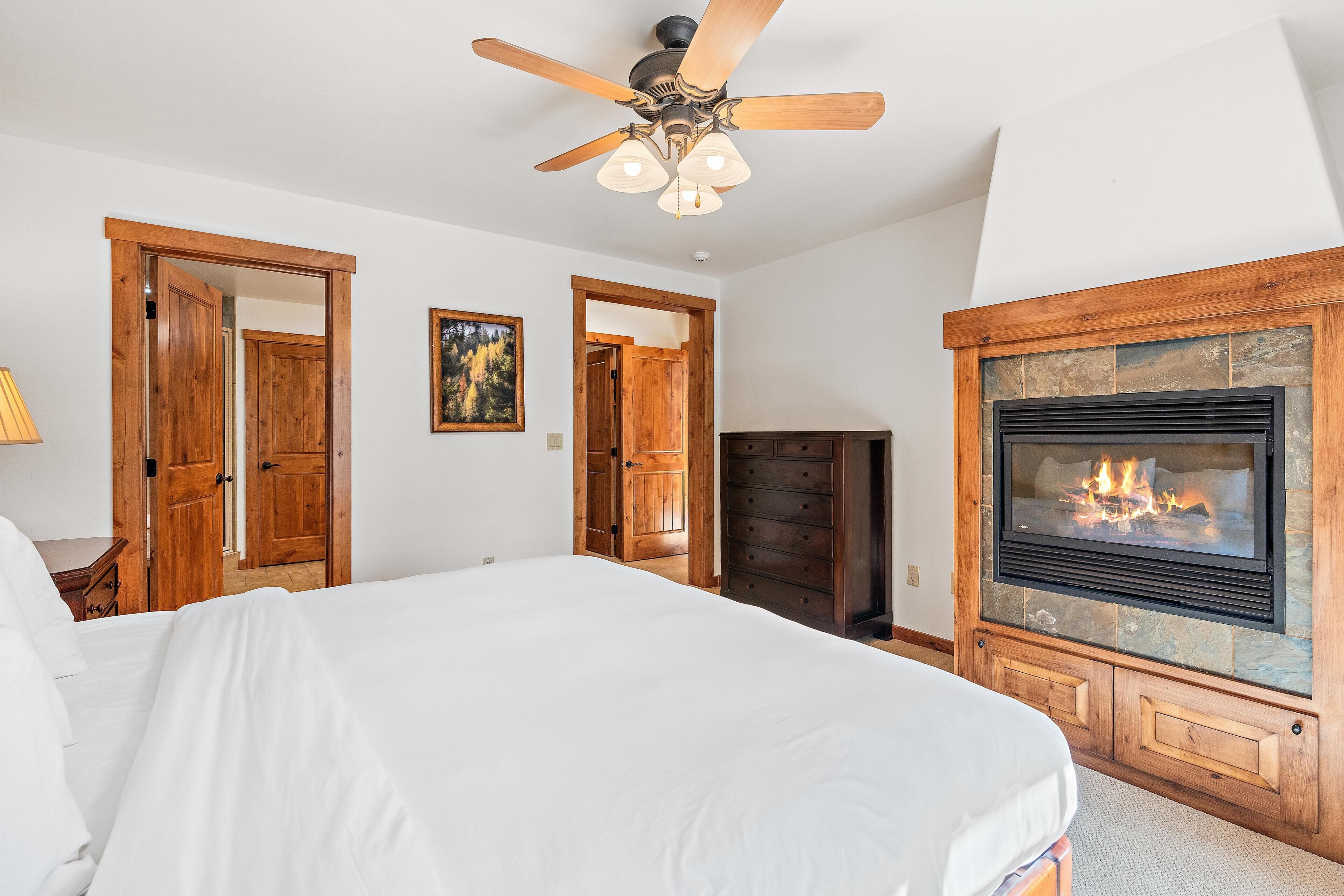 A bedroom with a bed, wooden doors, a fireplace, and a ceiling fan.
