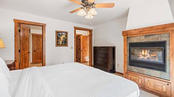 A bedroom with a bed, wooden doors, a fireplace, and a ceiling fan.