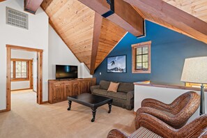 Ein Zimmer mit schrägem Dach, einem Fernseher, einer Couch, einem Korbstuhl und einem Holzschrank.