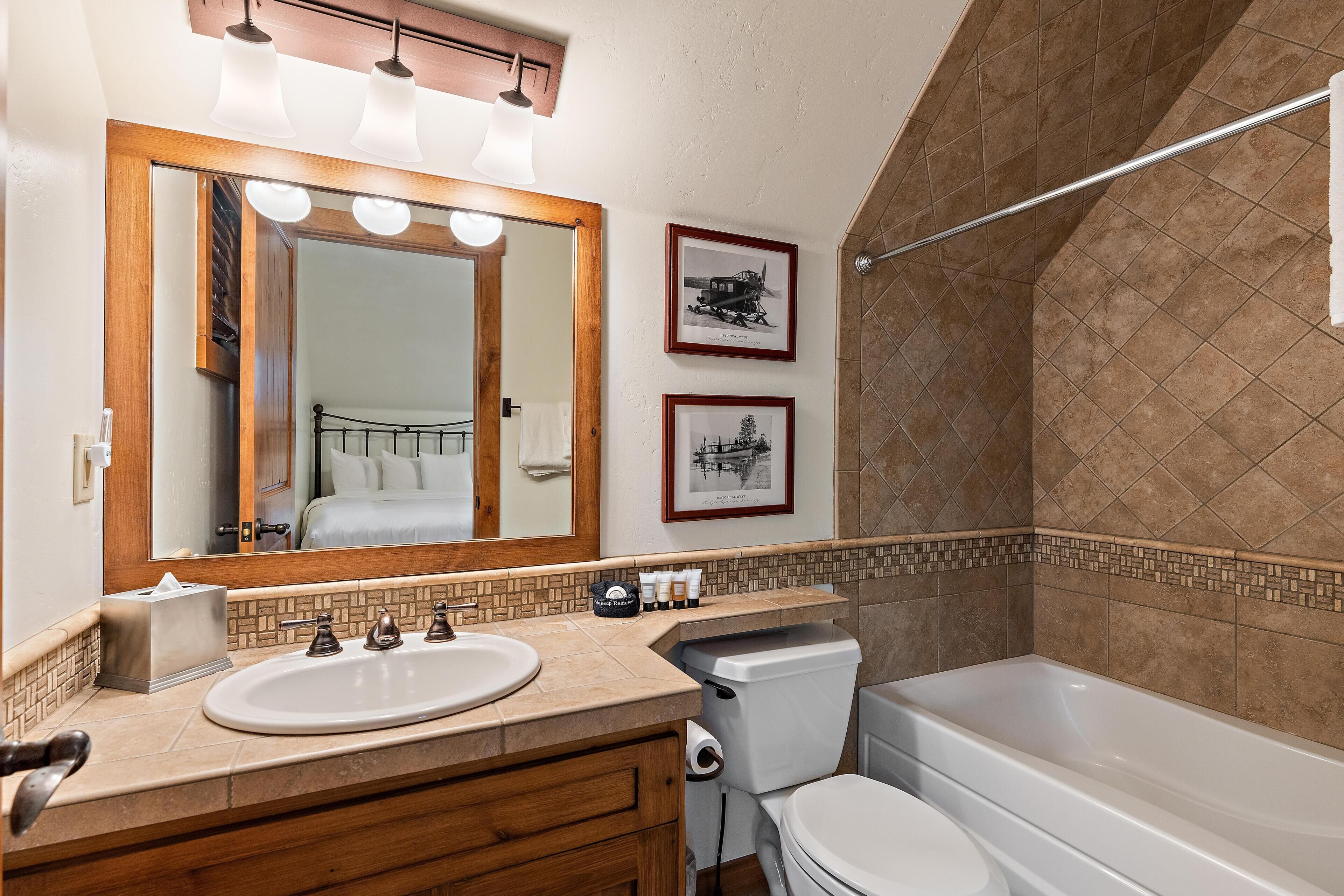 A bathroom with a large mirror, a sink, a toilet, and a bathtub. There are two framed pictures on the wall.