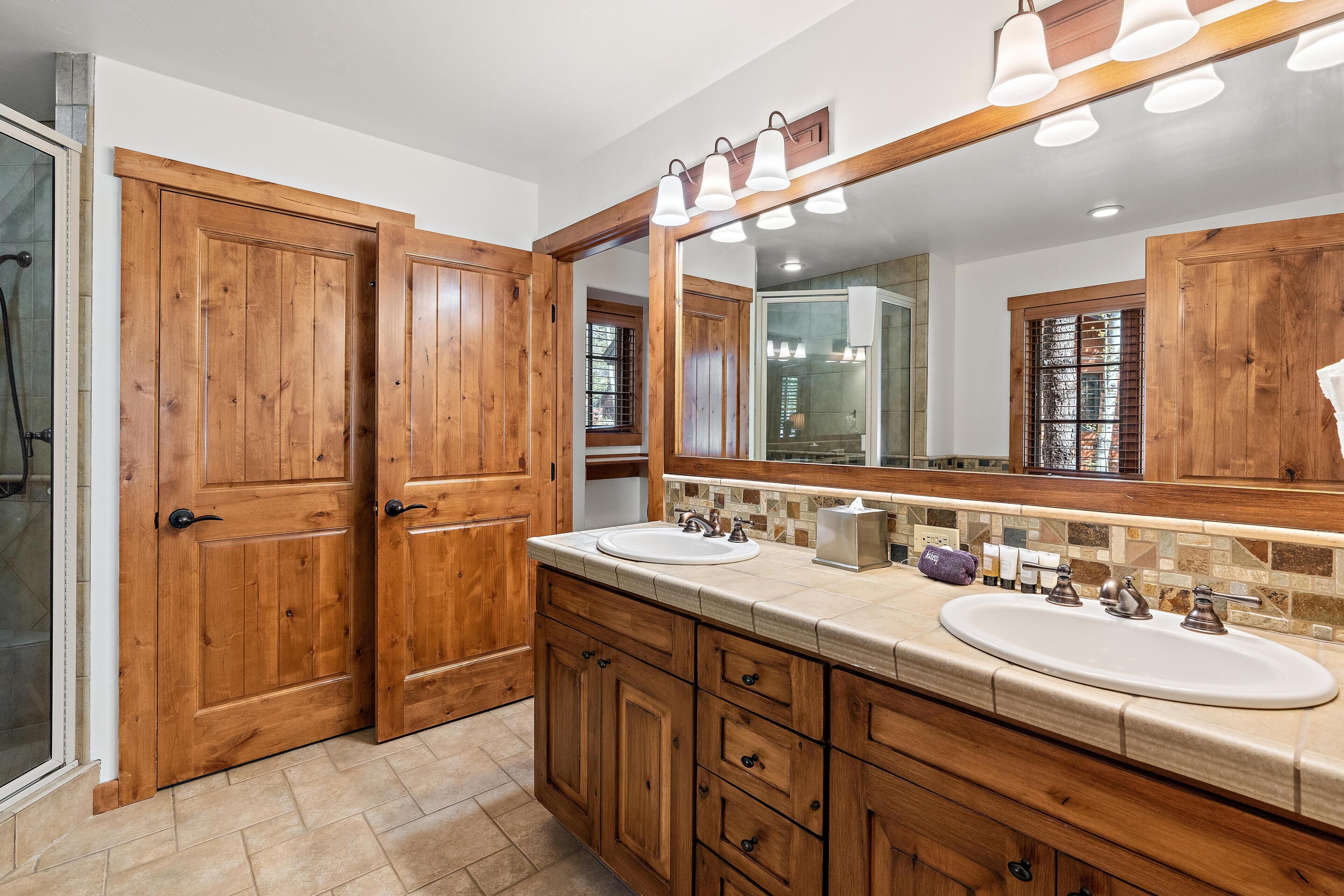 Un baño con muebles de madera, dos lavamanos, un espejo grande y una zona de ducha.