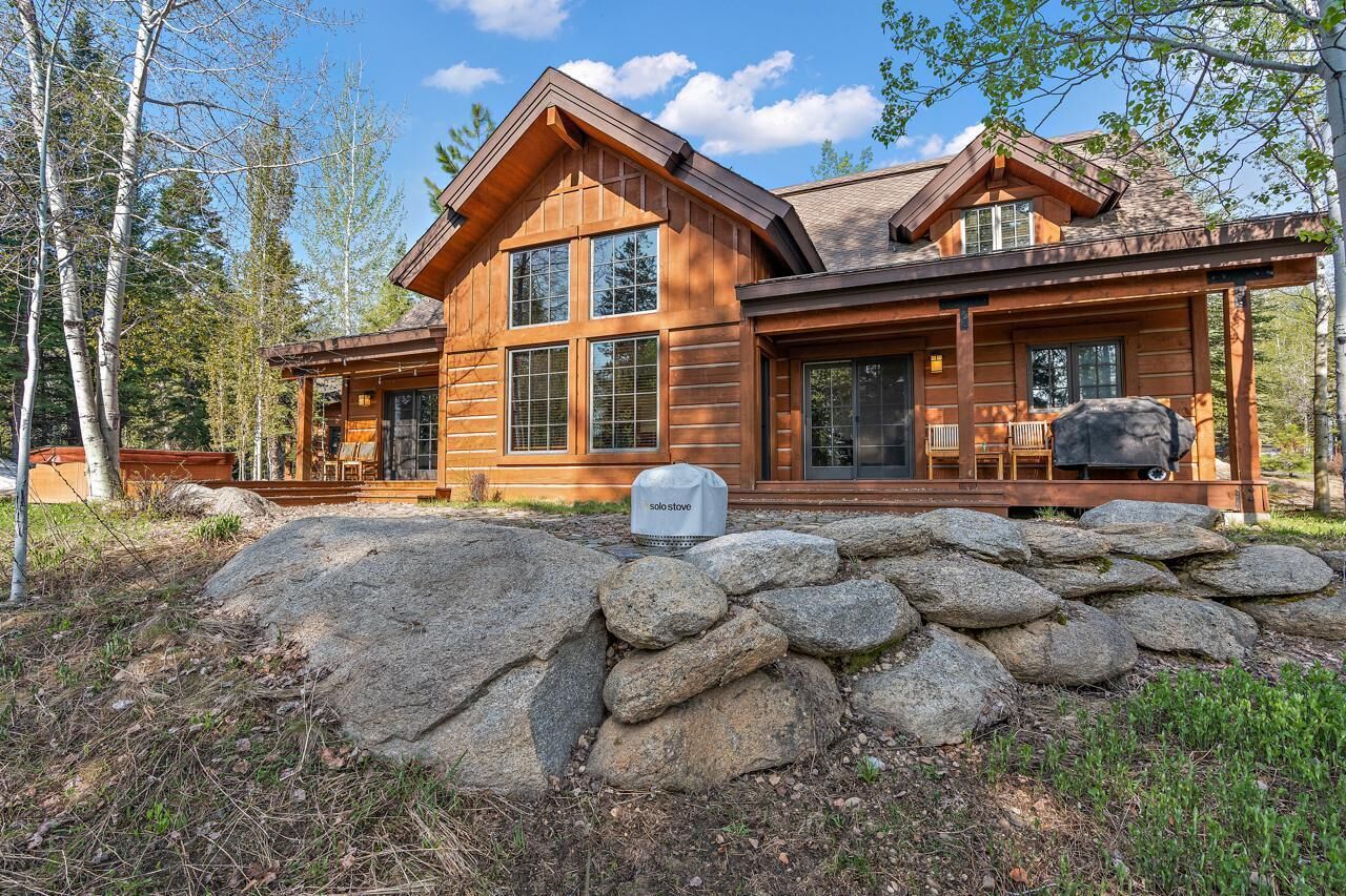 A log cabin with a stone foundation, large windows, and a covered porch.