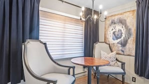 Een kamer met twee gestoffeerde stoelen, een ronde houten tafel en een kroonluchter.