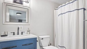 Een badkamer met een wit toilet, een blauwe wastafel en een witte douchegordijn met blauwe rand.