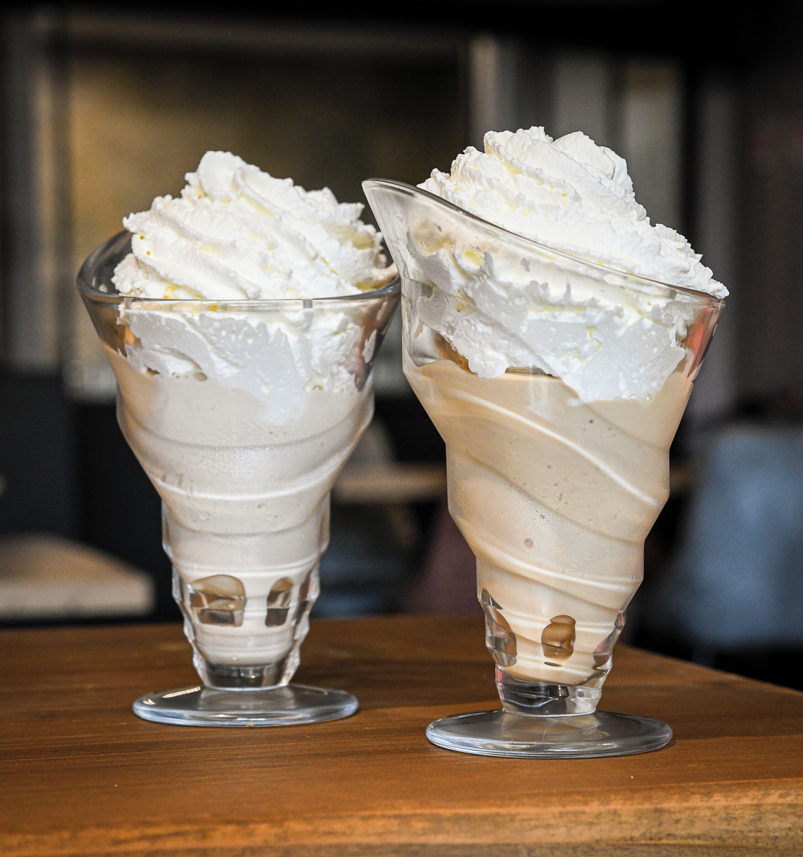 Dos vasos de postre con crema batida sobre una mesa de madera.