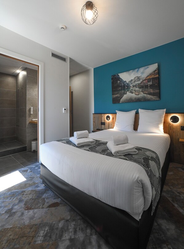 Une chambre d’hôtel moderne avec un grand lit, une douche et un tableau représentant un paysage montagneux.