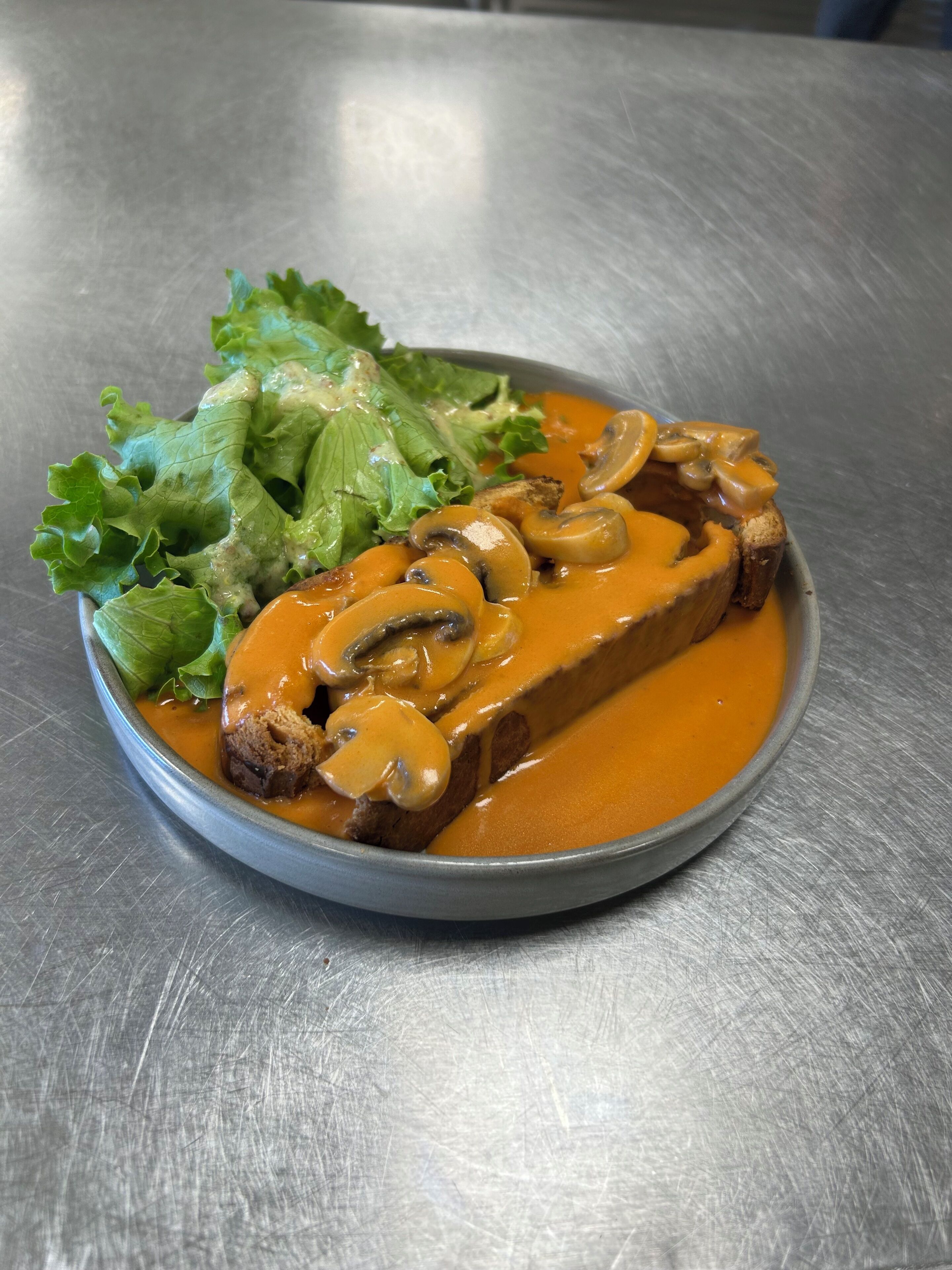 A plate of food with a slice of meat topped with mushrooms and sauce, accompanied by a side of green lettuce.