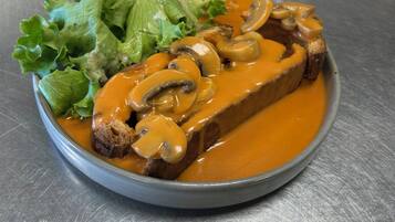 A plate of food with a slice of meat topped with mushrooms and sauce, accompanied by a side of green lettuce.