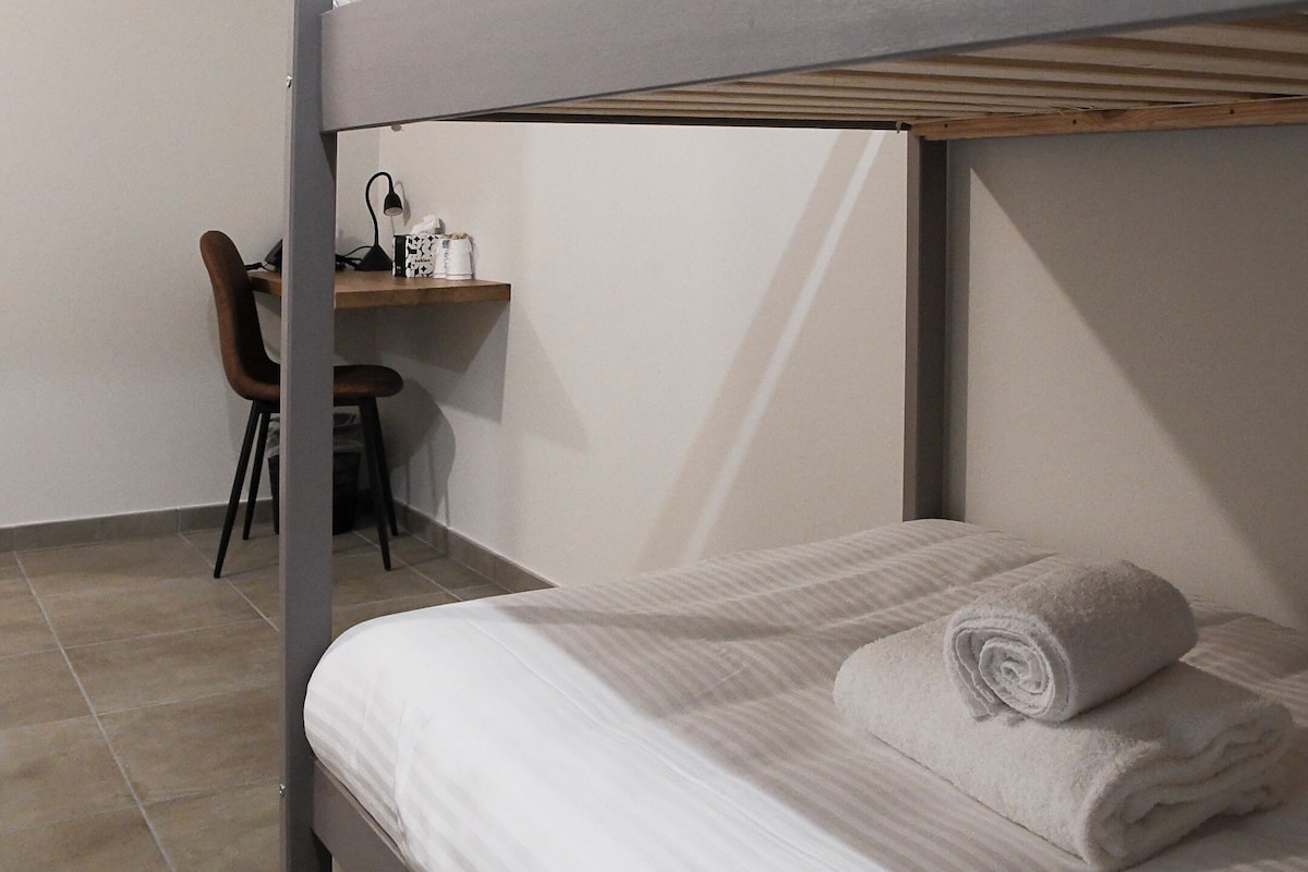 A bunk bed with a desk and chair in a room with tiled flooring.