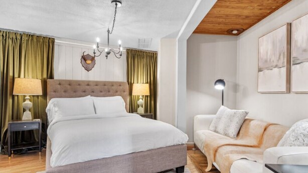 A modern bedroom with a large bed, a sofa, and a chandelier.