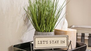 A sign with the text "LET'S STAY IN" placed on a tray next to a potted plant.