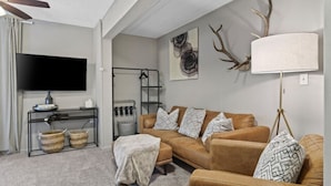 A living room with a brown sofa, a TV on a stand, a lamp, and wall art.