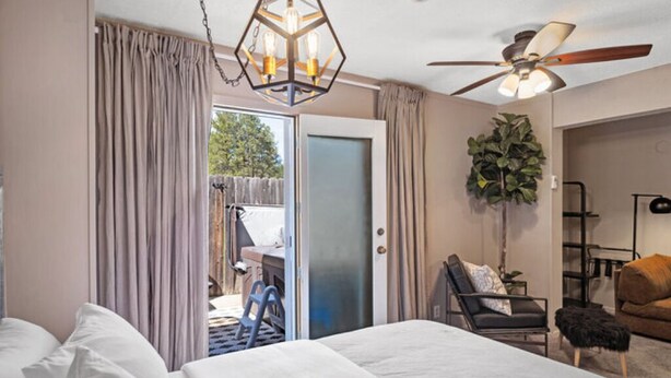 A hotel room with a bed, a ceiling fan, a chair, and a plant.