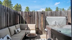 A backyard with a wooden fence, a hot tub, a sofa, and a small round table.