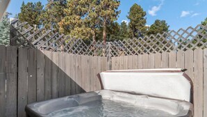 Ein Whirlpool in einem Garten mit Holzlattenzaun und Bäumen im Hintergrund.