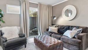 Ein Wohnzimmer mit einer Ledersofa, einem Knopf-Ottoman und einem runden Spiegel an der Wand.