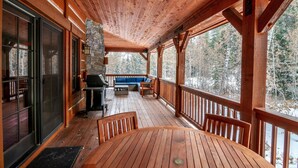 Un terrazzo in legno con un muro di pietra, un barbecue e un divano blu.