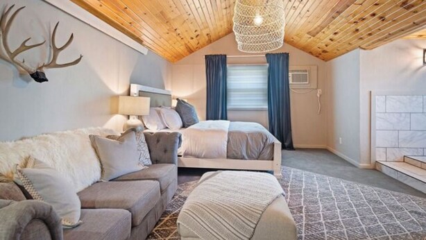 Un dormitorio acogedor con techo de madera, una cama, un sofá y un adorno de asta en la pared.