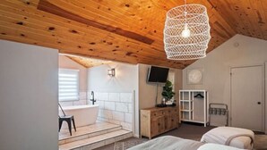 Un dormitorio con dos camas, techo de madera, lavamanos blanco y un televisor.