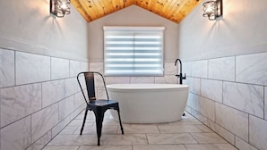 Un baño con una bañera independiente, una silla y una ventana con persianas.