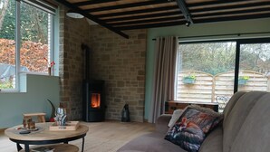 A cozy living room with a stone wall, a fireplace, a round wooden table, and a comfortable sofa. - Évasion nature au Loft du Renard –  Calme et vue boisée près de Namur (Namur)