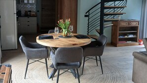 A dining area with a round wooden table, six chairs, and a central vase with flowers. - Évasion nature au Loft du Renard –  Calme et vue boisée près de Namur (Namur)