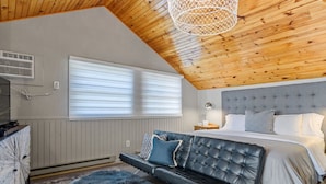 Ein Schlafzimmer mit Holzboden, einem Bett mit weißer Bettwäsche, einem schwarzen Ledersofa und einem flauschigen Teppich.