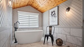Ein modernes Badezimmer mit einer freistehenden Badewanne, einem Sessel und einer Zierblume.