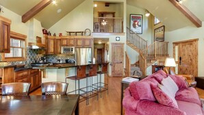 A spacious kitchen with wooden cabinets, a dining area with a table and chairs, and a living room with a pink sofa. - Serene Chalet|Private Hot Tub|Wood Fireplace (Tamarack)