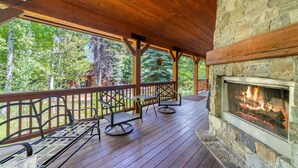 A covered deck with wooden flooring, stone walls, and a stone fireplace.