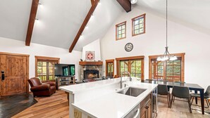 A spacious kitchen with a large island, wooden beams, and a stone fireplace.