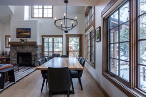 A spacious dining area with a long wooden table, black chairs, and a stone fireplace. - Comfortable 2 Bedroom Townhome  | Ski in/Ski Out (Tamarack)