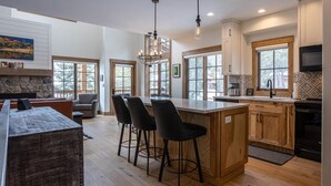 A modern kitchen with a large island, bar stools, and a stone fireplace.