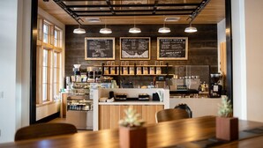 A modern cafe with wooden tables and chairs, a counter with coffee machines, and menu boards on the wall.