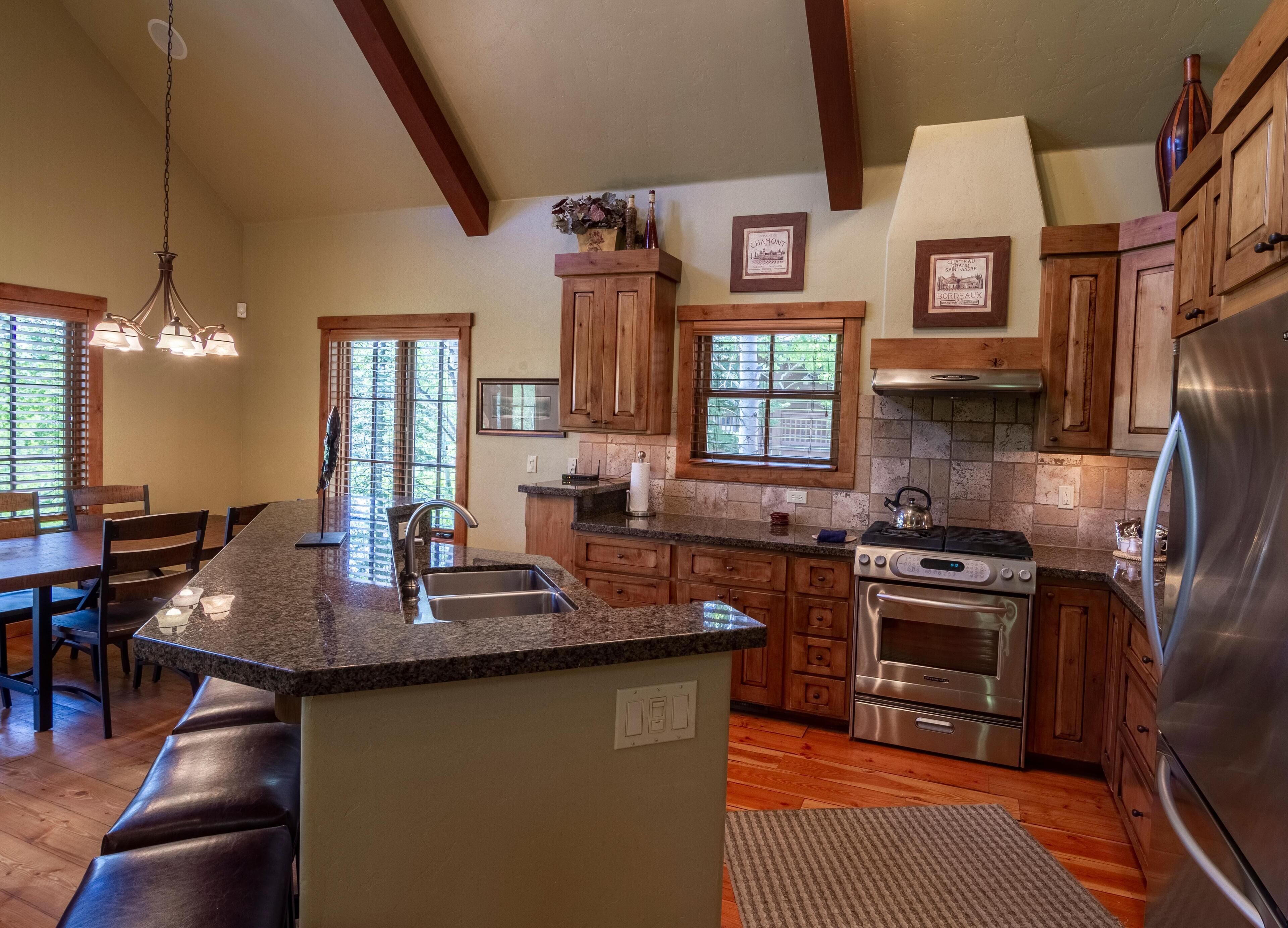 A spacious kitchen with granite countertops, wooden cabinets, a stainless steel refrigerator, and a large island with a sink.