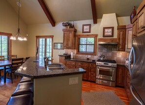 A spacious kitchen with granite countertops, wooden cabinets, a stainless steel refrigerator, and a large island with a sink.