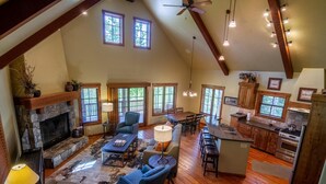 A spacious living area with a stone fireplace, wooden beams, and a high ceiling. - Peaceful Chalet |Private Hot Tub, Wood Fireplace (Tamarack)