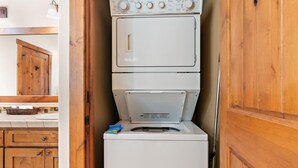 Een kleine wasruimte met gestapelde wasmachines en drogers, houten kastjes en een aanrecht met een mand.