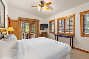 Une chambre d’hôtel avec un grand lit, un ventilateur de plafond, une télévision et des fenêtres avec des cadres en bois.