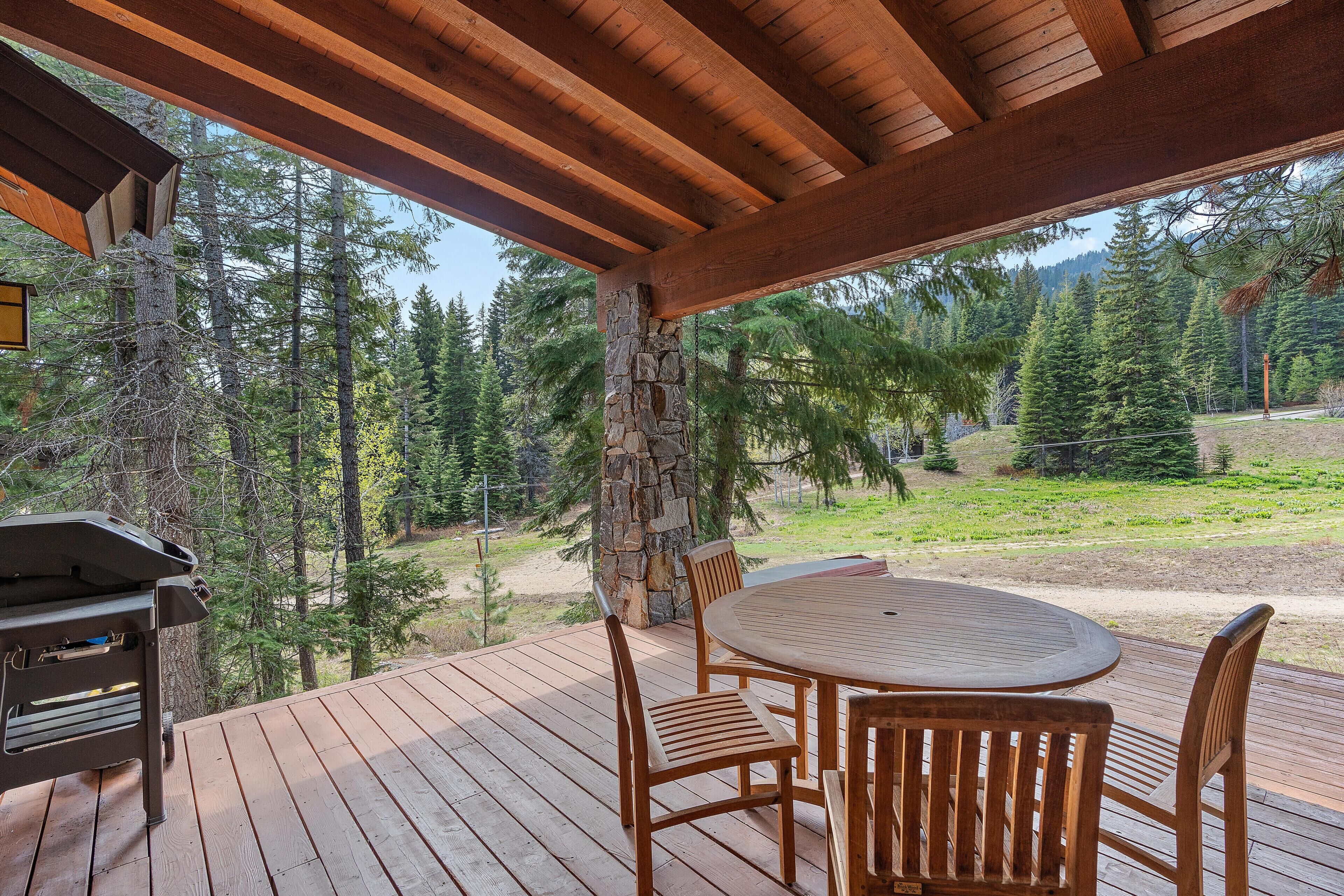 A wooden deck with a stone pillar, a grill, and a round table with chairs.