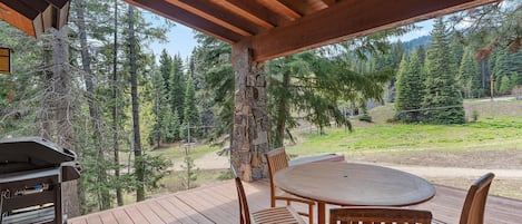 A wooden deck with a stone pillar, a grill, and a round table with chairs.