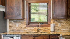 A kitchen with a granite countertop, wooden cabinets, a window with blinds, and a stainless steel dishwasher.